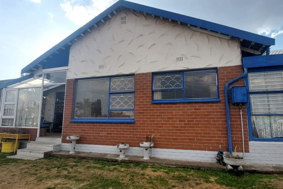 Rear view of a brick house featuring a textured gable, blue-painted window frames with security bars, and concrete steps leading to the entrance.