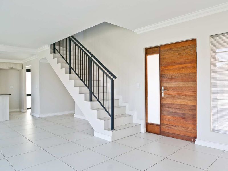 Bright and modern entrance hall featuring a timber front door, tiled flooring, and a staircase with a sleek metal balustrade.