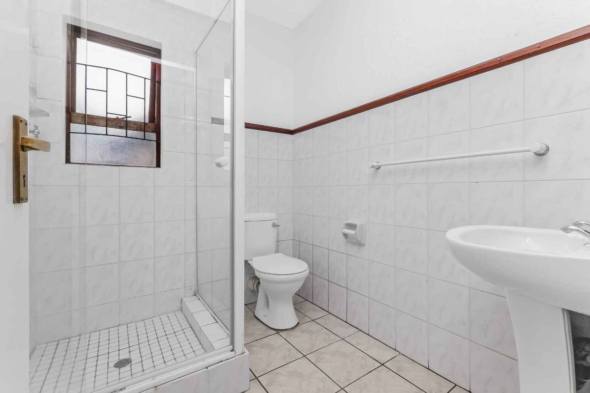 A functional bathroom featuring a glass-enclosed shower, pedestal sink, and white wall tiling with a decorative trim.