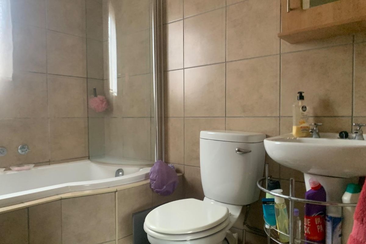 A functional bathroom featuring a built-in bathtub with a glass shower screen, a pedestal basin, and a standard toilet with neutral wall tiling.