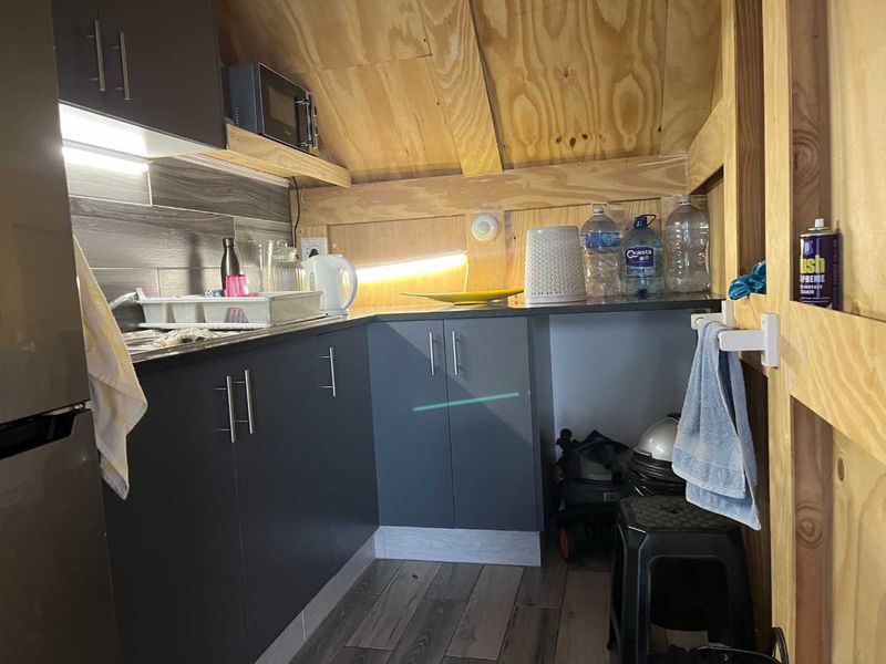 Compact kitchen area featuring modern dark cabinetry, tiled backsplash, and exposed plywood ceiling structure, providing a functional and efficient workspace.