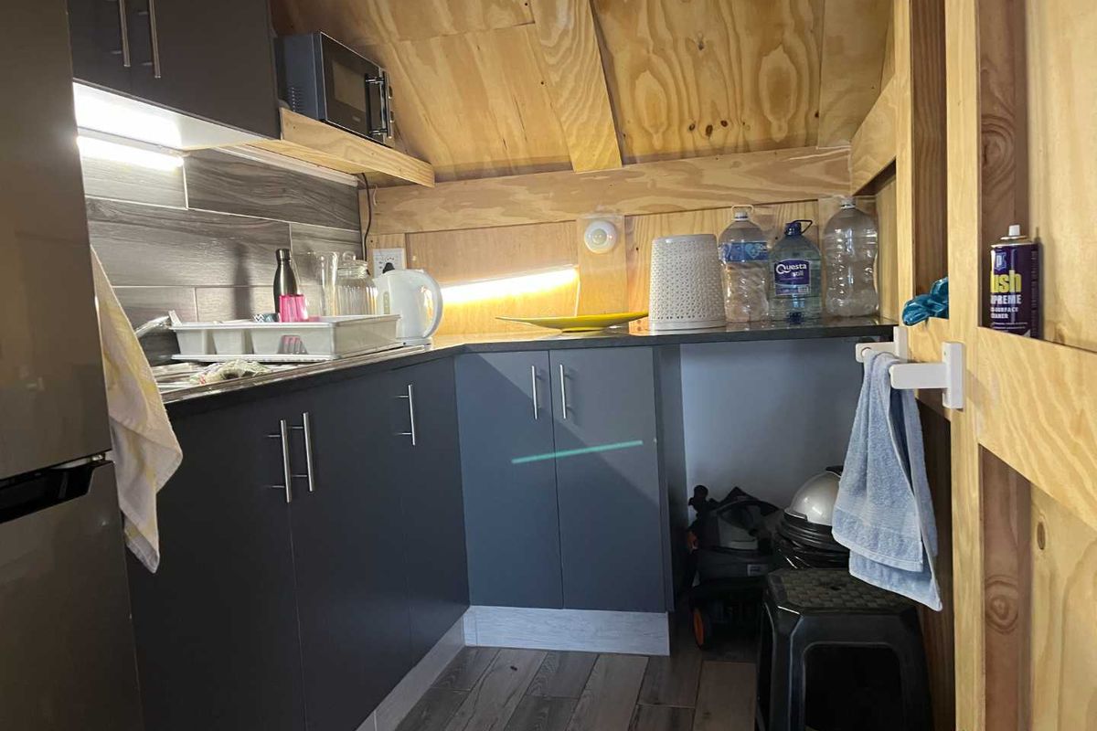 Compact kitchen area featuring modern dark cabinetry, tiled backsplash, and exposed plywood ceiling structure, providing a functional and efficient workspace.