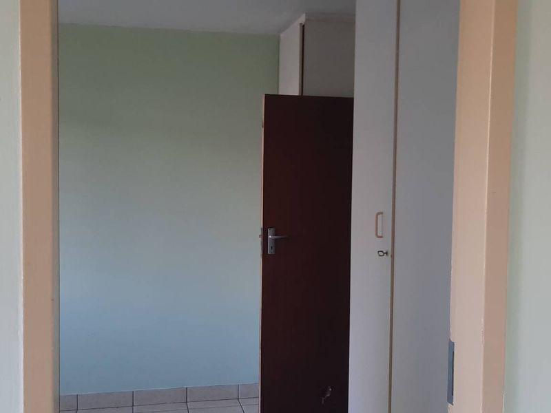 An empty bedroom featuring built-in cupboards and tiled flooring, viewed through an open doorway.