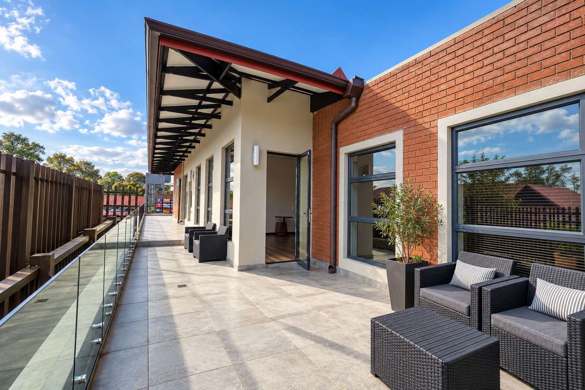 A spacious, modern balcony featuring tiled flooring, a sleek glass balustrade, and an exposed steel roof structure, providing a clean outdoor office transition space.