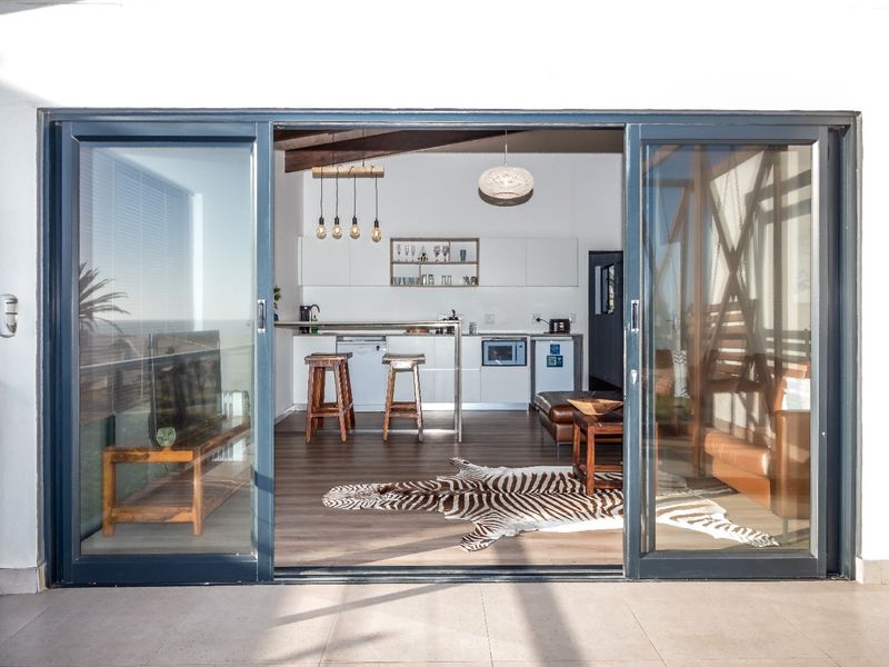 An open-plan living and kitchen area featuring exposed timber beams, modern cabinetry, and a breakfast bar, seamlessly connected to a tiled outdoor patio.