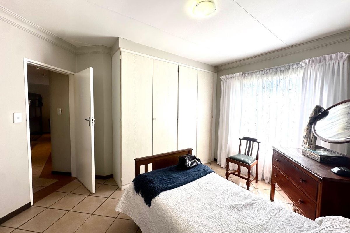 A bedroom featuring built-in cupboards, tiled flooring, and natural light through a window with curtains.