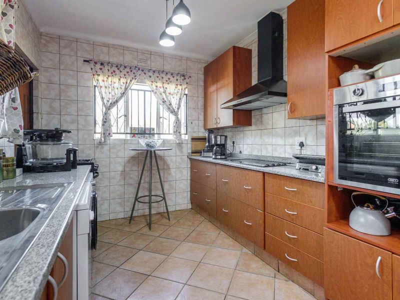 Functional kitchen featuring wooden cabinetry, granite countertops, built-in oven, extractor fan, and tiled finishes throughout.