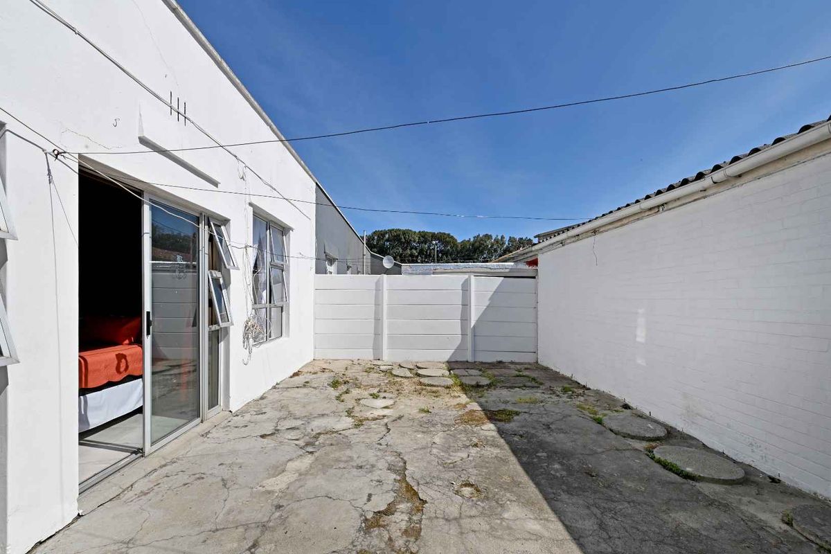 A rear exterior courtyard featuring a concrete patio area, enclosed by painted brick and precast boundary walls with access via a sliding glass door.