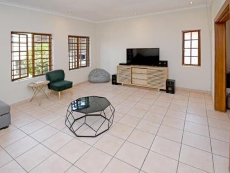 Spacious living room featuring neutral tiled flooring, recessed downlighting, and large windows fitted with security bars.