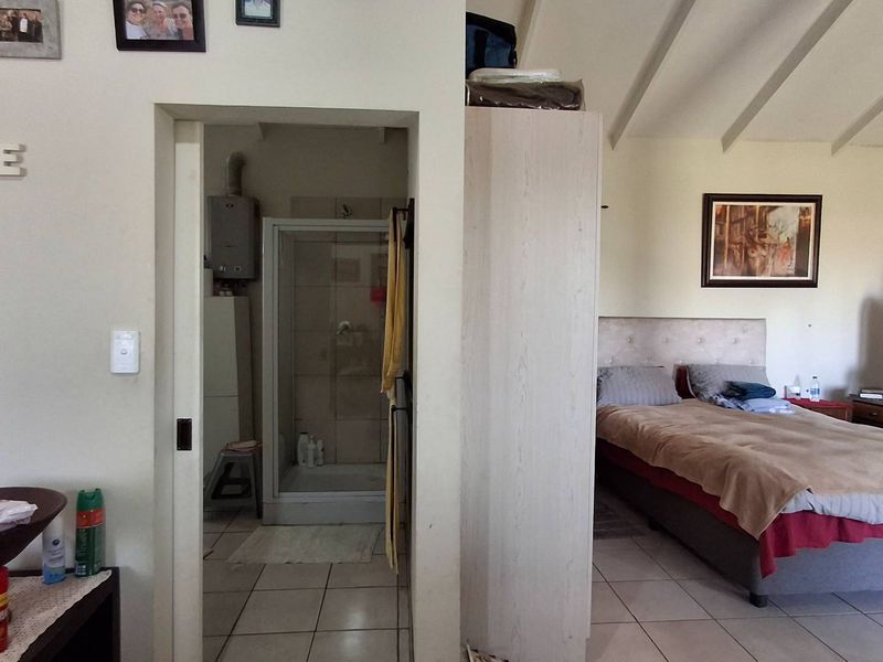 Spacious bedroom featuring vaulted ceilings, tiled flooring, and an en-suite bathroom with a shower and gas geyser installation.