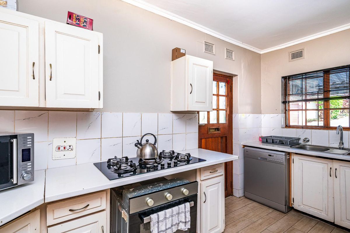 Functional kitchen featuring white cabinetry, built-in gas hob, oven, and tiled splashbacks with direct access to the exterior.