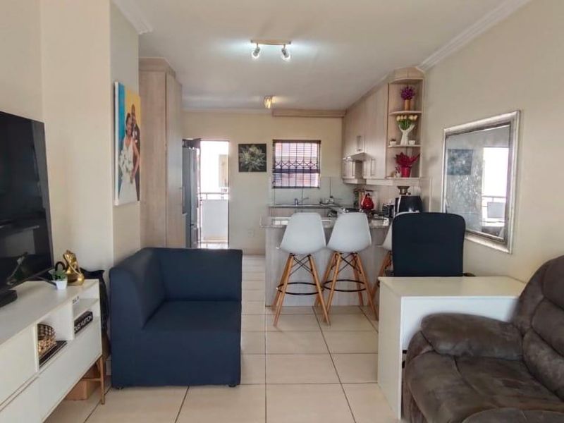 Open-plan living and kitchen area featuring tiled flooring, neutral cabinetry, and a breakfast bar, creating a functional and connected living space.