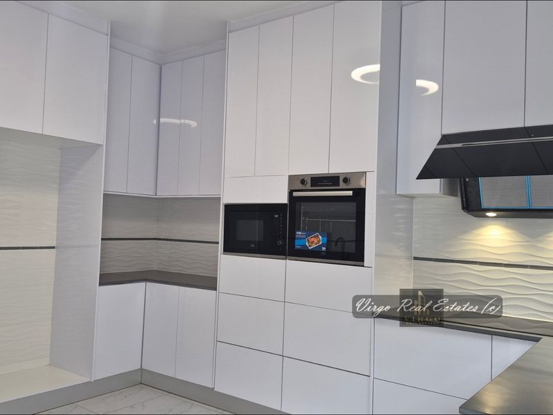 Modern kitchen featuring high-gloss white cabinetry, integrated oven and microwave, sleek extractor fan, and textured tile backsplash with stone countertops.