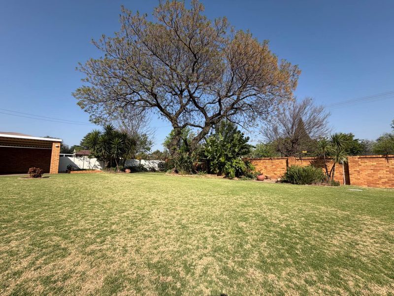 A spacious, well-maintained garden featuring a large lawn, mature trees, and secure brick boundary walls.
