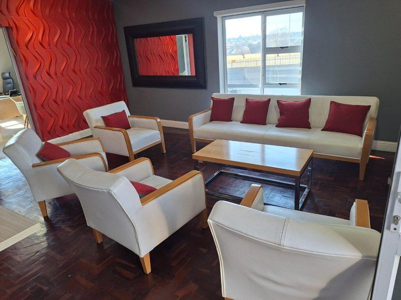 A living room featuring dark parquet flooring, a bold red textured feature wall, and a large window providing natural light.