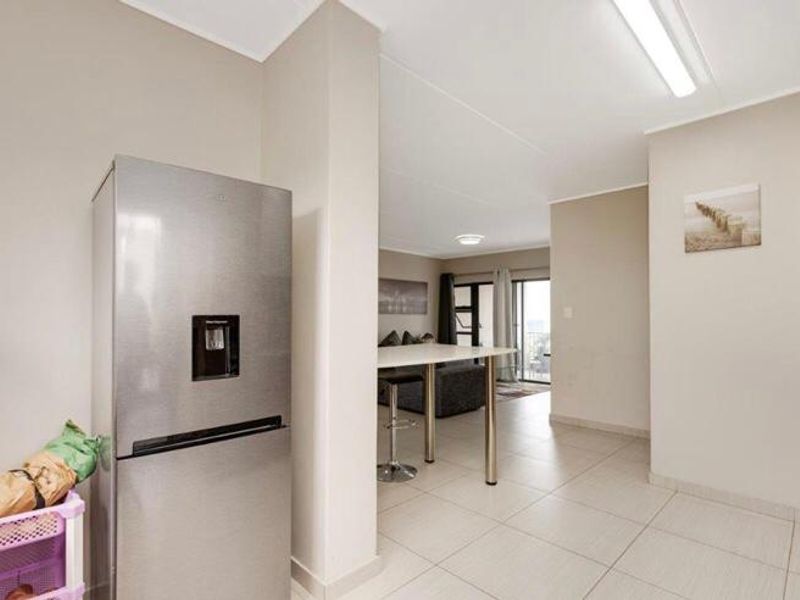 An open-plan living area featuring tiled flooring and a breakfast bar, connecting the kitchen space to the lounge area.