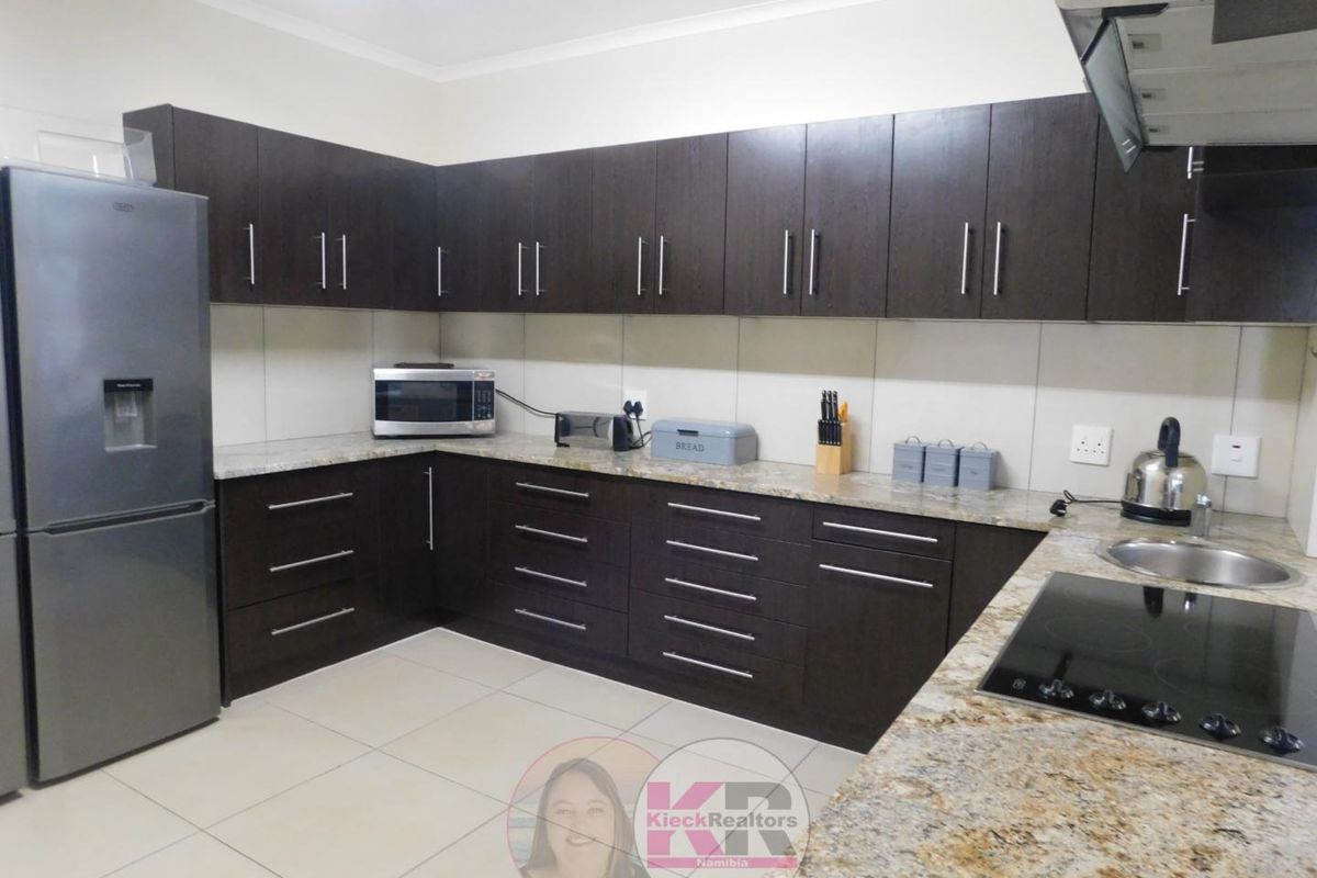 Modern kitchen featuring dark wood cabinetry, granite countertops, tiled backsplash, and integrated electric hob with extractor fan.