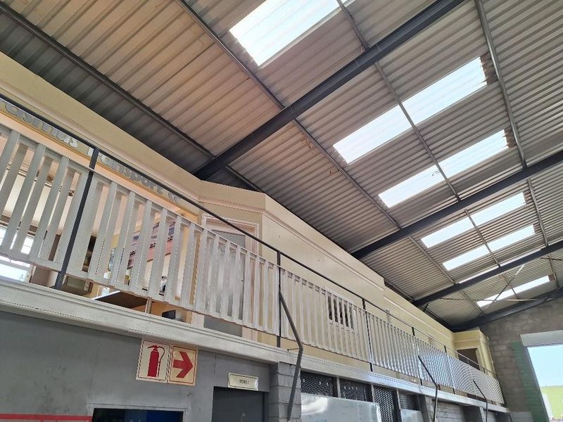 Industrial warehouse space featuring a mezzanine level with safety railing, high-pitched metal roofing, and integrated skylights for natural illumination.