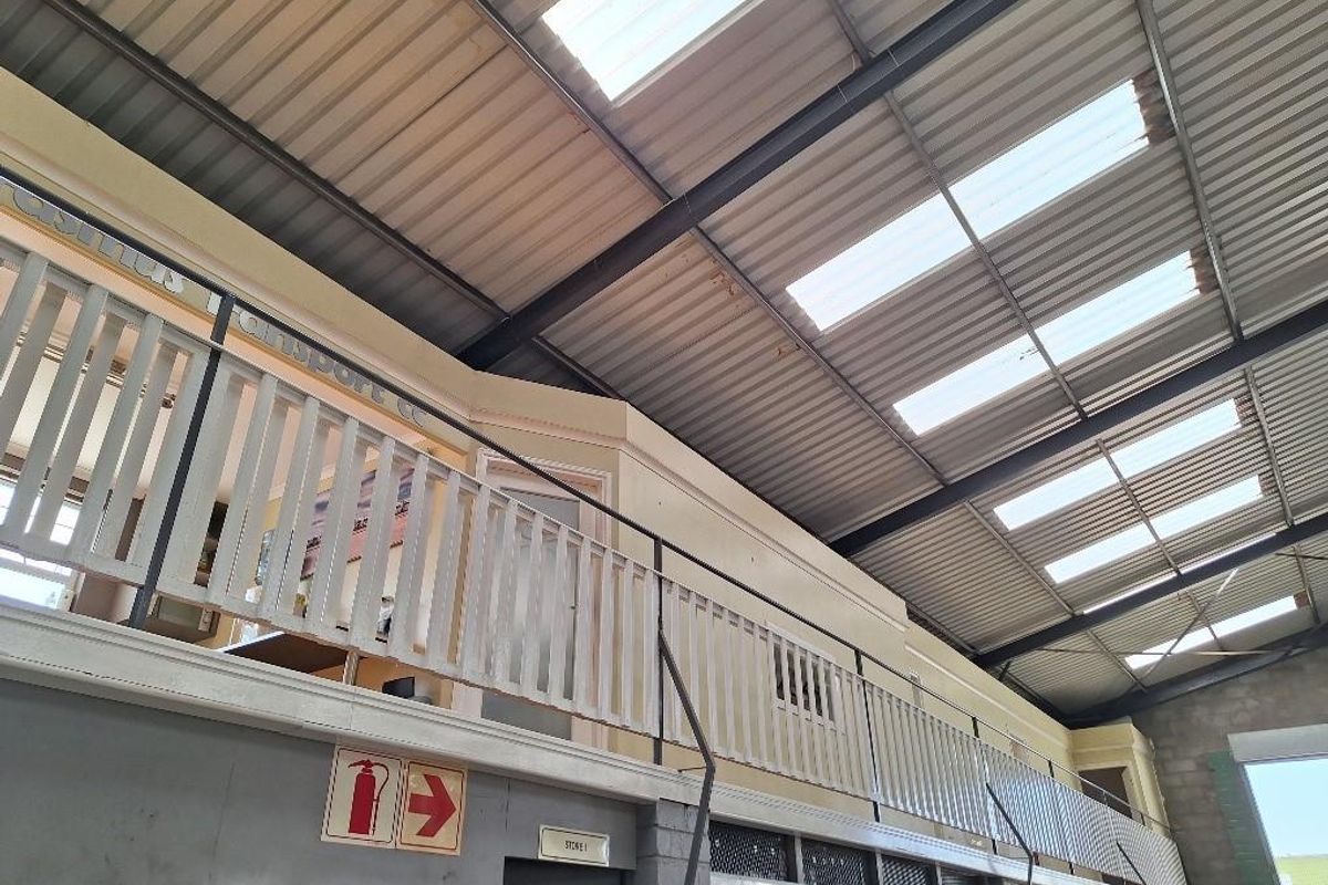 Industrial warehouse space featuring a mezzanine level with safety railing, high-pitched metal roofing, and integrated skylights for natural illumination.