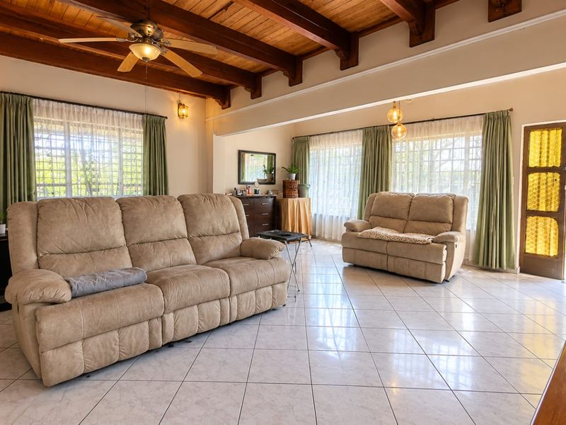 Spacious living room featuring exposed timber beam ceilings, ceramic floor tiles, and large windows that provide ample natural light.