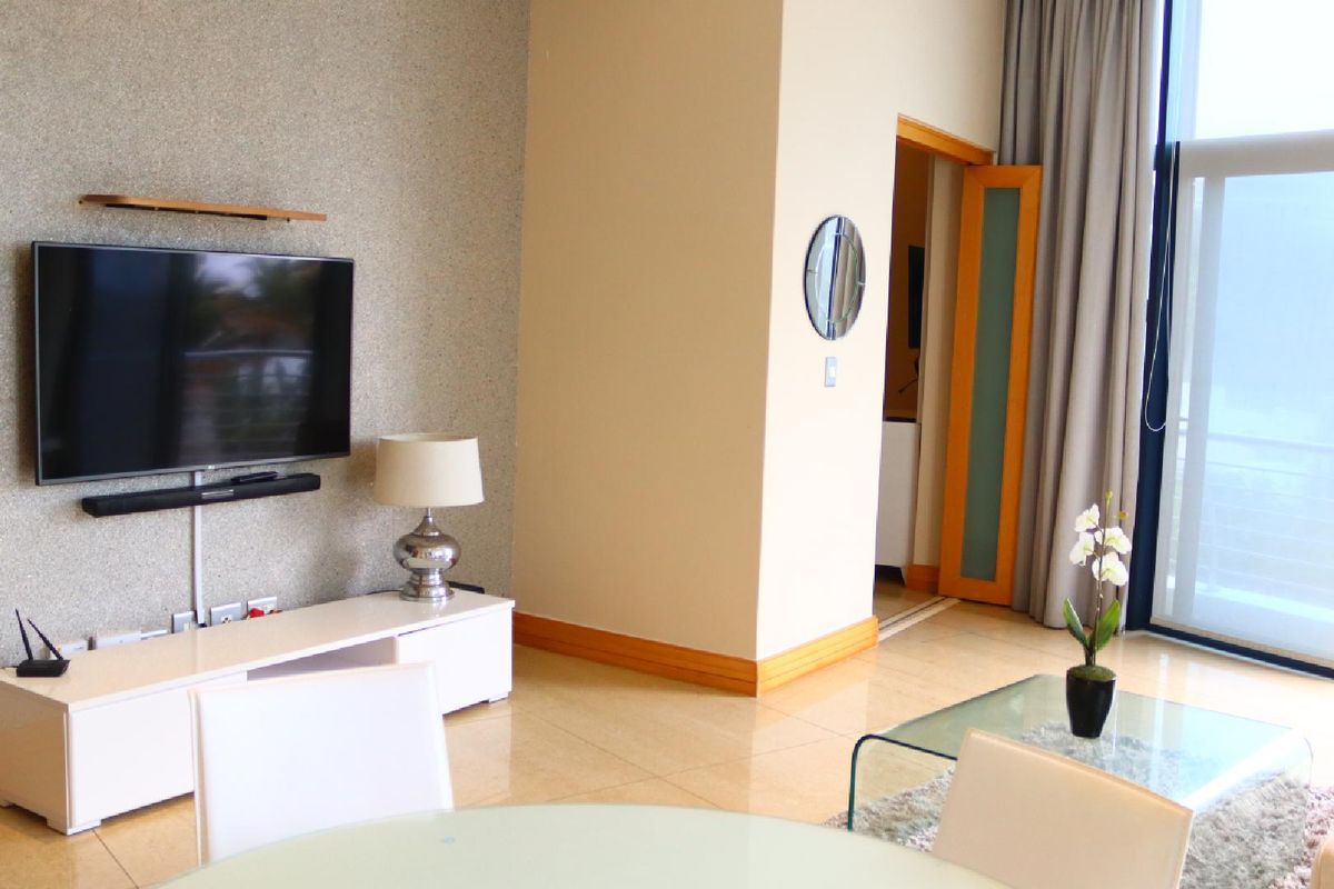 A bright living room featuring tiled flooring, a textured feature wall, and floor-to-ceiling windows with access to a balcony.