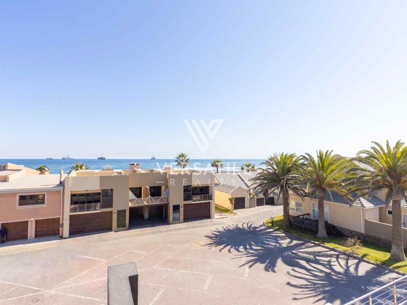 Aerial view of a residential complex featuring paved driveways, multiple garage units, and balconies with a clear ocean view.