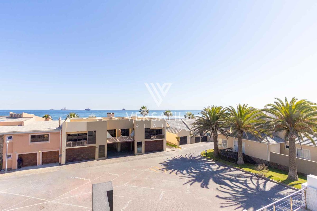 Aerial view of a residential complex featuring paved driveways, multiple garage units, and balconies with a clear ocean view.