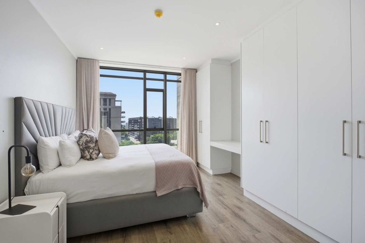Modern bedroom featuring floor-to-ceiling windows, built-in white cabinetry with integrated desk space, and wood-look flooring.