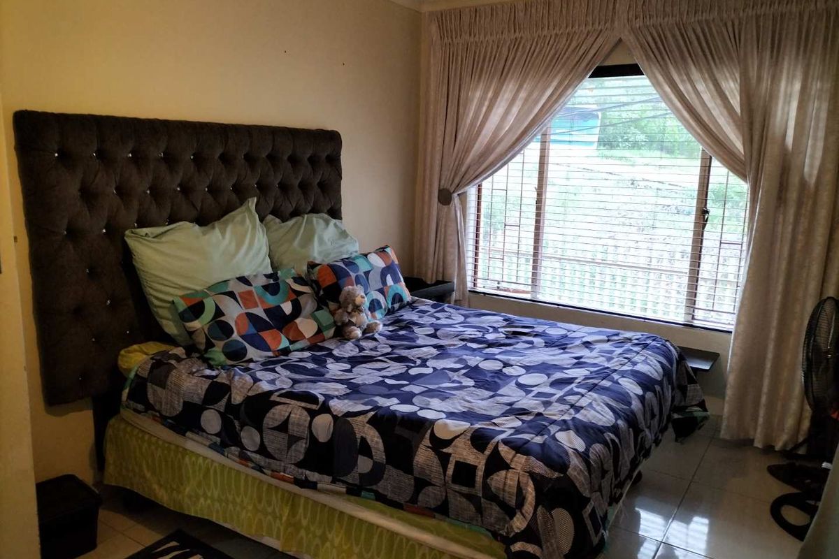 A bedroom featuring tiled flooring, a large window with fitted curtains, and a neutral wall finish.