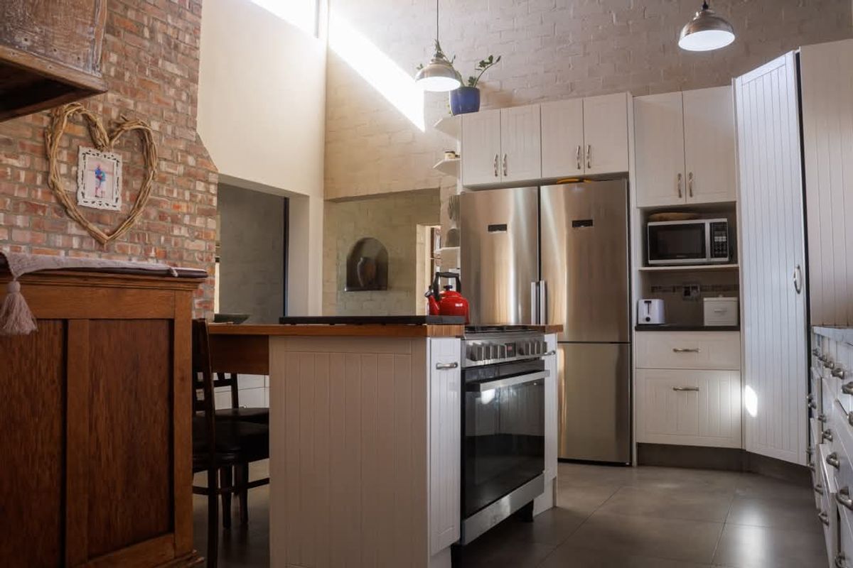 A spacious kitchen featuring white cabinetry, a central island with a built-in oven, and a striking exposed brick feature wall with high ceilings.