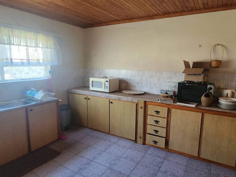 A functional kitchen featuring laminate cabinetry, double stainless steel sink, tiled splashback, and timber ceiling, offering potential for modern renovation.