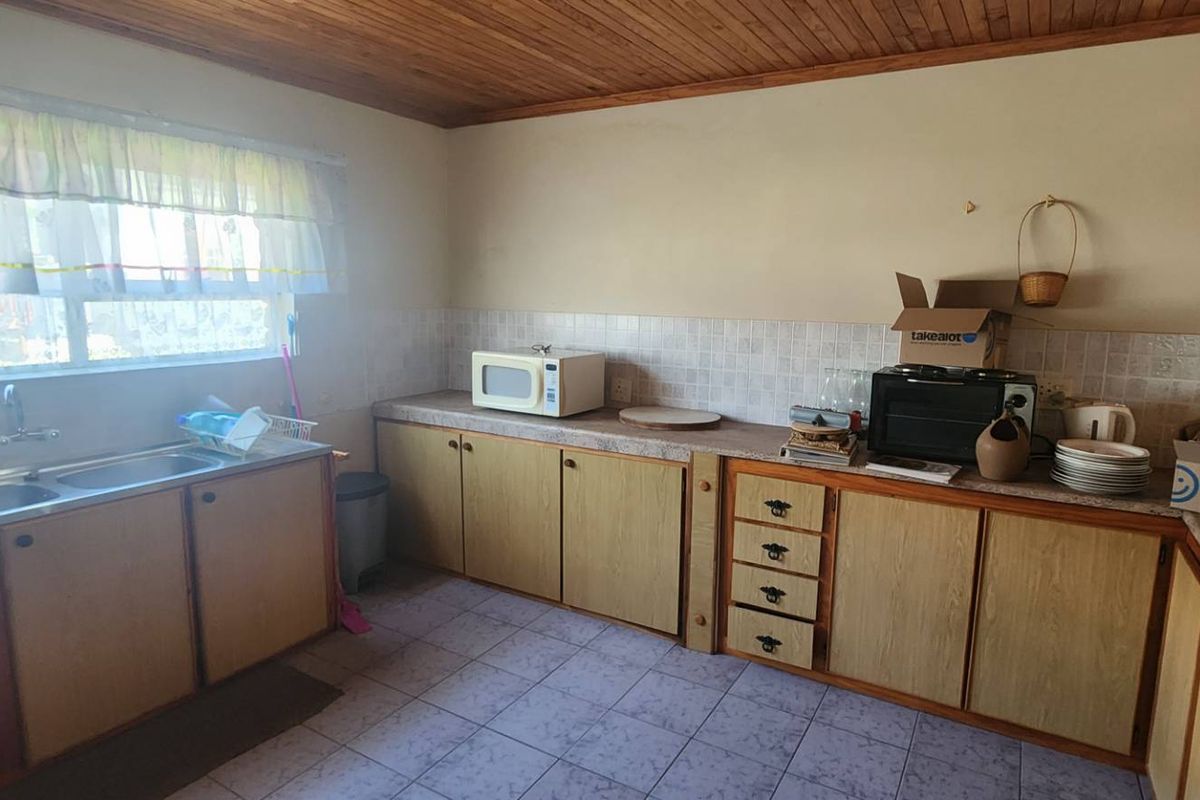 A functional kitchen featuring laminate cabinetry, double stainless steel sink, tiled splashback, and timber ceiling, offering potential for modern renovation.