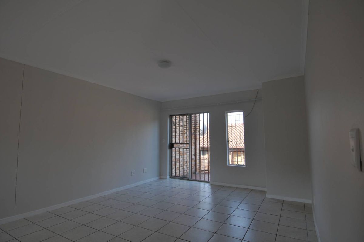 An empty living room featuring tiled flooring, a sliding glass door with security gate, and a separate window providing natural light.