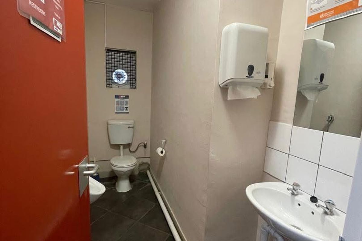 A functional office restroom featuring a pedestal sink, toilet, and tiled flooring with visible exposed plumbing.