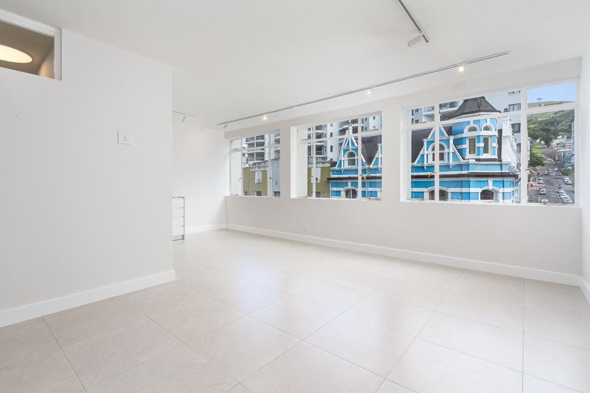 A bright, spacious, and empty living area featuring large windows, modern tiled flooring, and track lighting, offering a clean canvas for interior design.