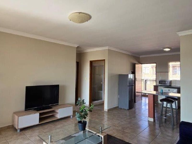 Open-plan living area featuring tiled flooring, ceiling cornicing, and a kitchen breakfast bar, creating a functional and connected living space.