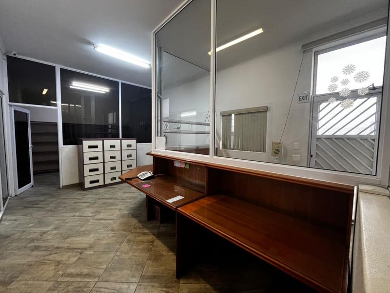 Functional office reception area featuring a built-in wooden desk, glass partition, and tiled flooring, suitable for administrative or industrial business operations.