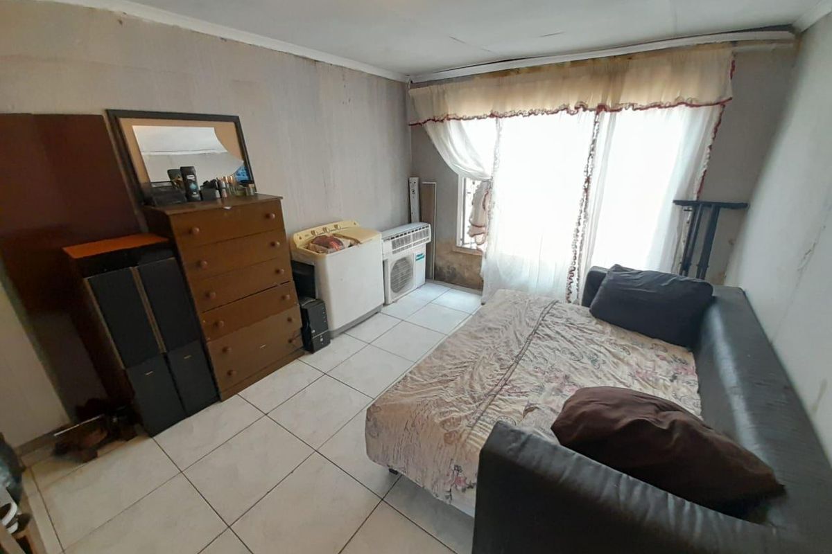 A bedroom featuring tiled flooring and a large window with curtains, requiring cosmetic updates to the wall finishes.