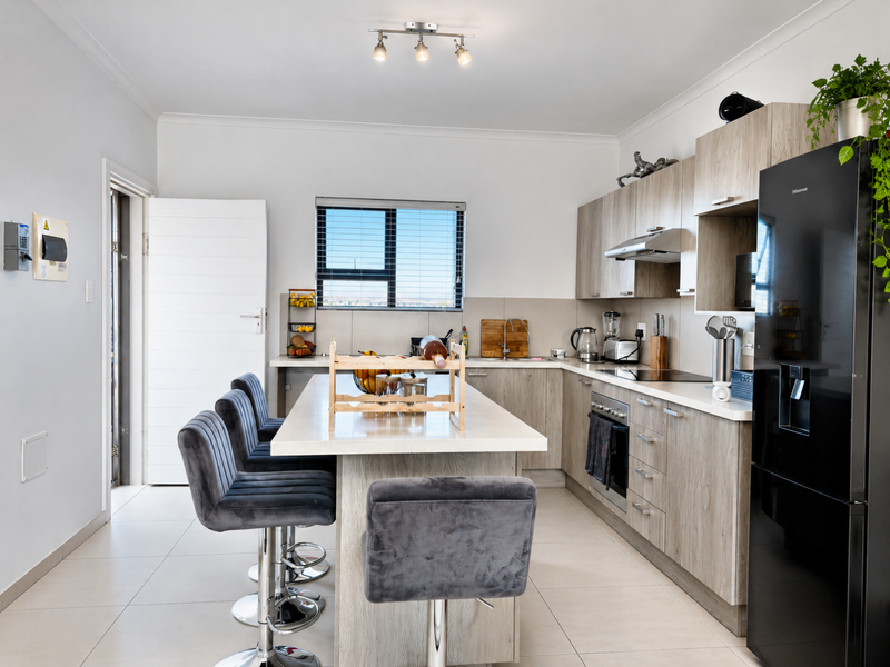 Modern kitchen featuring light wood-grain cabinetry, stone countertops, a central island, and integrated appliances, finished with neutral floor tiles.