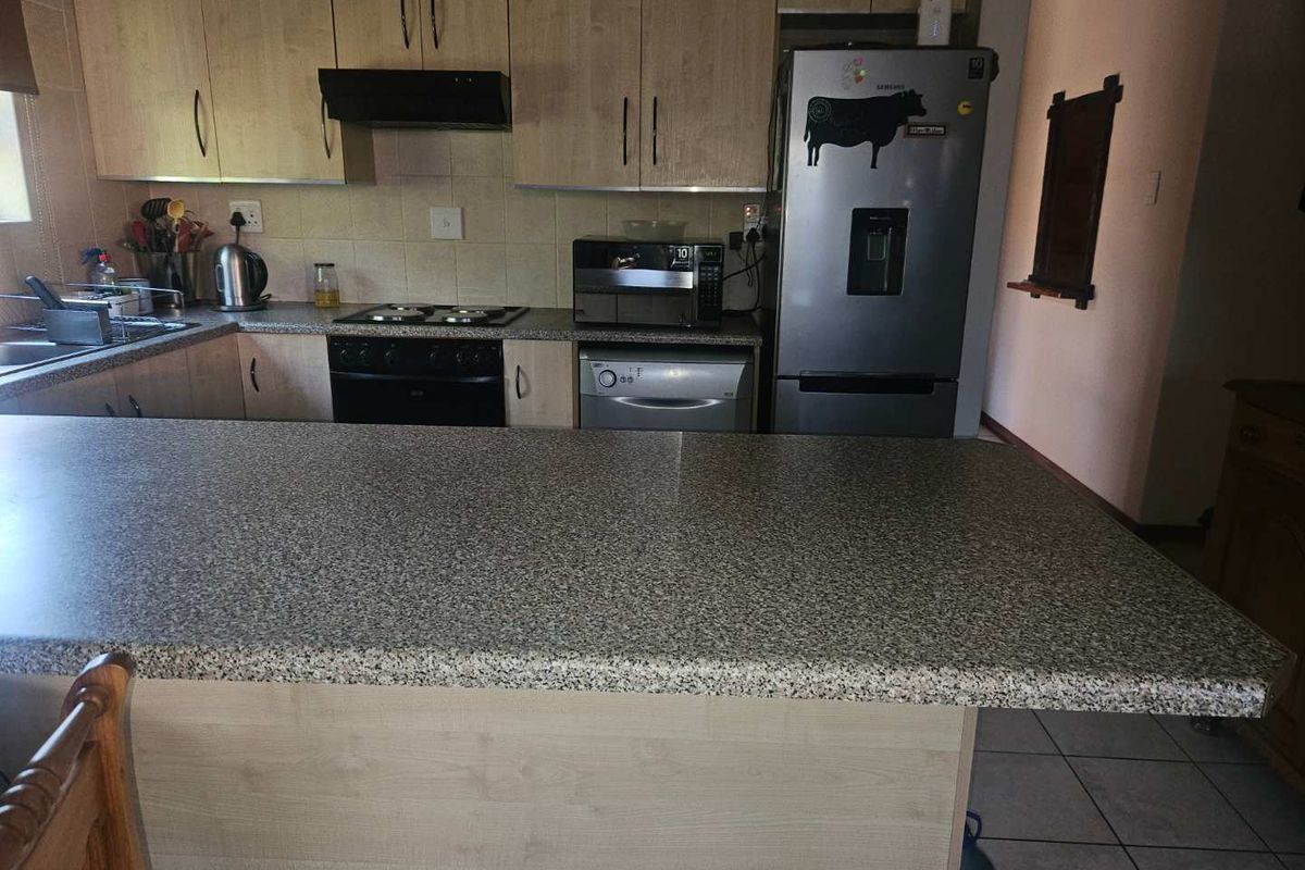 A functional kitchen featuring light wood cabinetry, granite-look laminate countertops, a breakfast bar, and built-in stove with extractor fan.