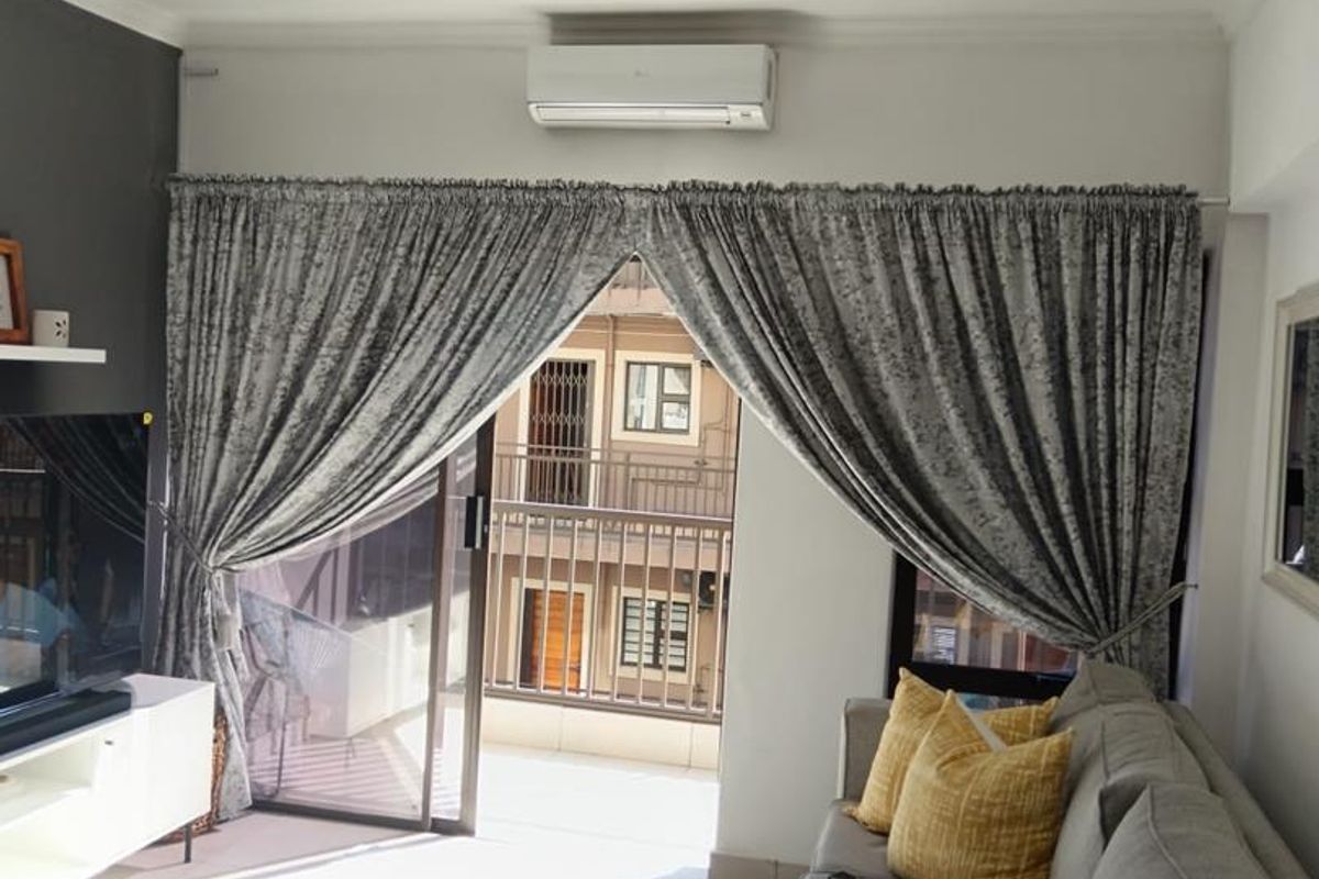 A well-maintained living room featuring a split-system air conditioner, an accent wall, and a sliding glass door providing access to a balcony.