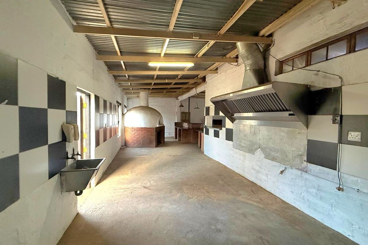 Spacious industrial-style kitchen featuring a built-in brick pizza oven, large stainless steel extractor hood, and wall-mounted sink, suitable for commercial or catering use.