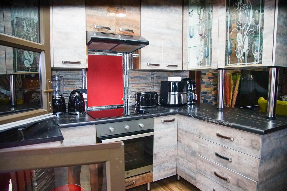 A compact kitchen featuring wood-look cabinetry, dark stone-effect countertops, a built-in oven, electric hob, and a modern extractor fan.