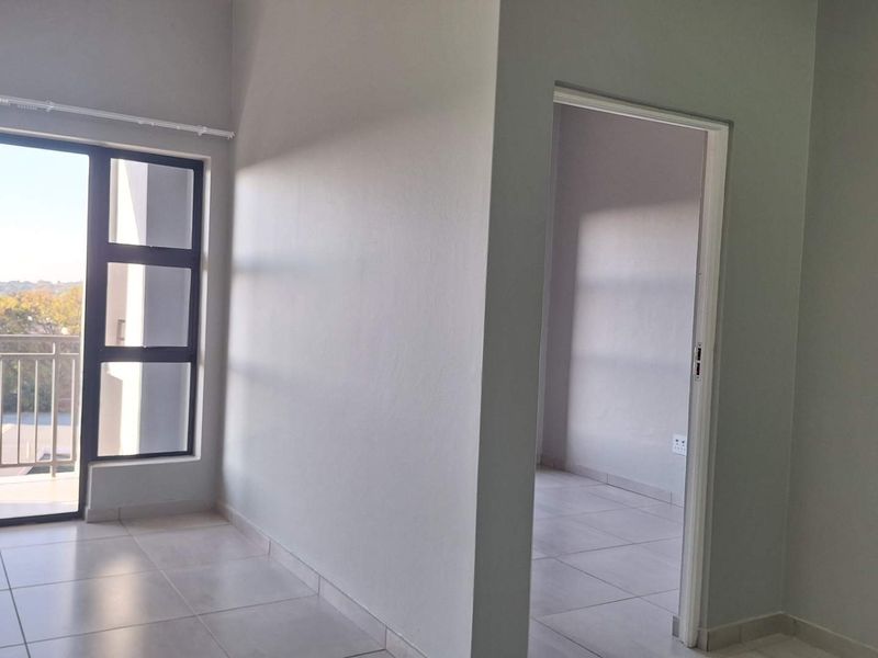 An empty, well-lit living area featuring neutral tiled flooring and a large sliding glass door leading to a balcony.