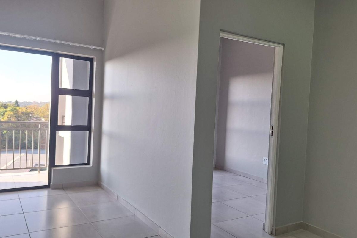 An empty, well-lit living area featuring neutral tiled flooring and a large sliding glass door leading to a balcony.