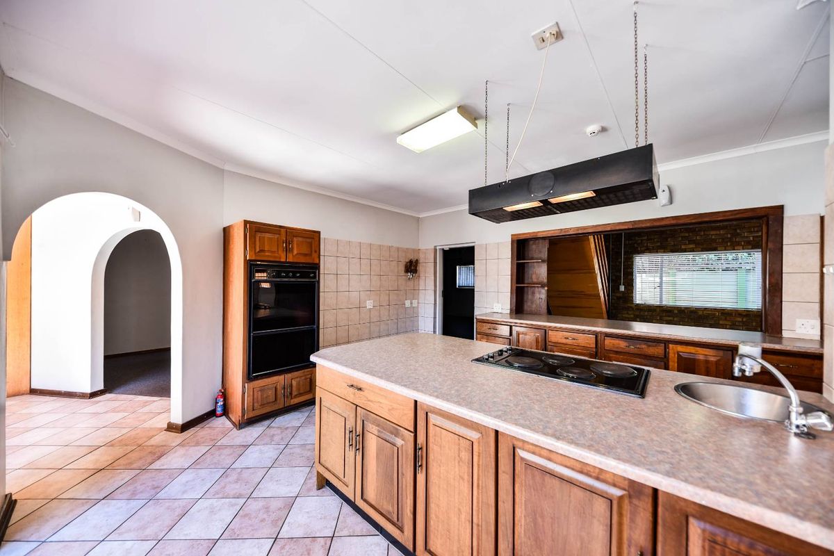A spacious kitchen featuring a central island with a built-in hob, wooden cabinetry, tiled flooring, and a distinctive arched entryway.