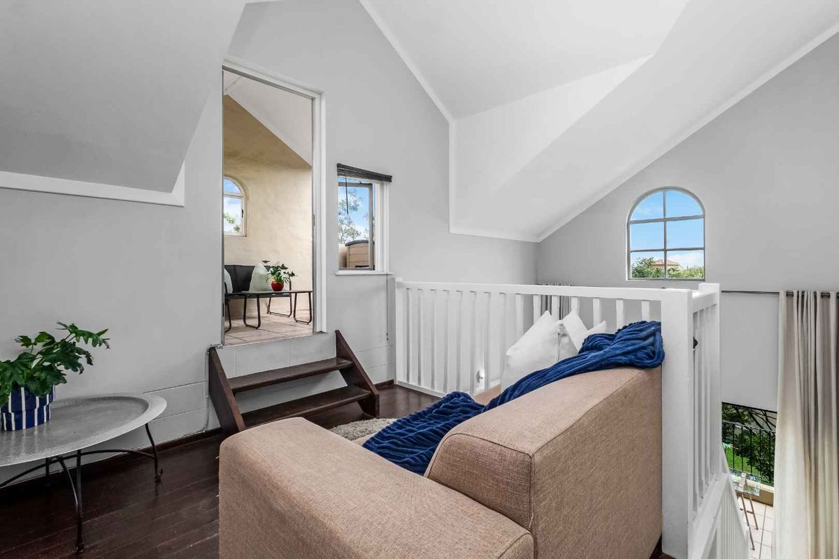 A bright loft-style living area featuring vaulted ceilings, a white balustrade, arched window, and direct access to an outdoor balcony space.