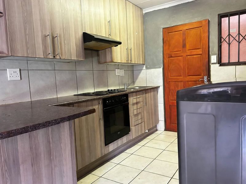 Functional kitchen featuring wood-look cabinetry, built-in oven and hob, tiled backsplash, and direct access to an exterior door.