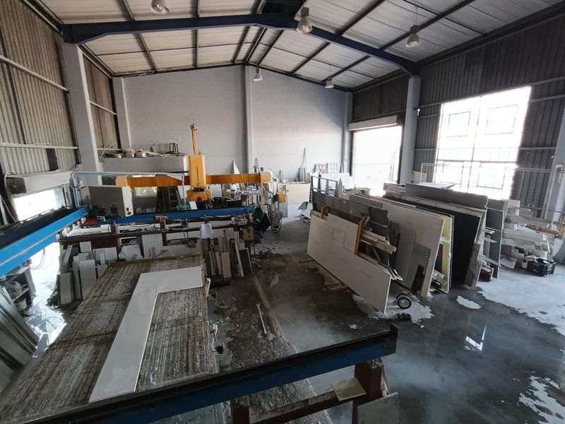 Industrial workshop space featuring high ceilings, concrete flooring, and large roller shutter access, currently utilized for stone fabrication and processing.