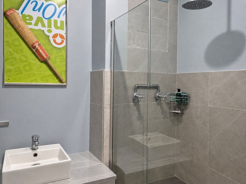 Modern bathroom featuring a glass-enclosed shower with a rain shower head, a sleek countertop basin, and contemporary grey wall tiling.